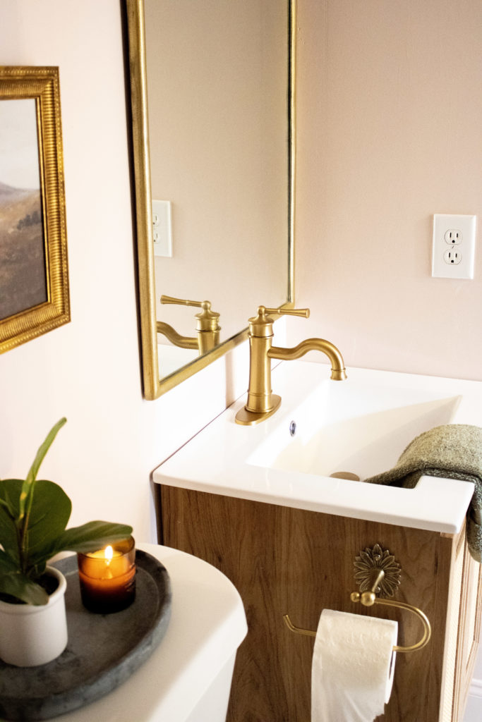 Pink bathroom with a cane and white vanity, gold faucet, and vintage style mirror. 