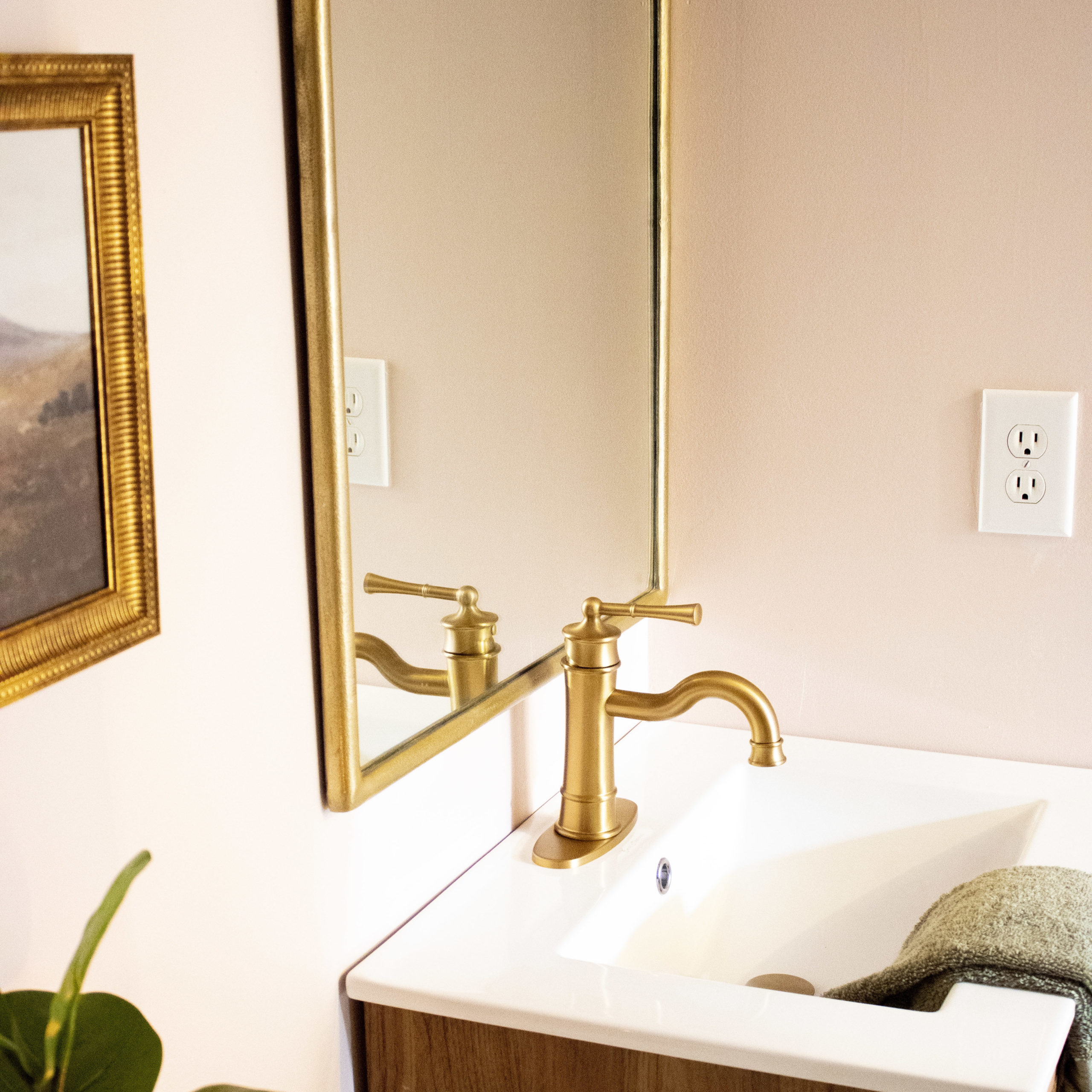 Pink bathroom with a cane and white vanity, gold faucet, and vintage style mirror.