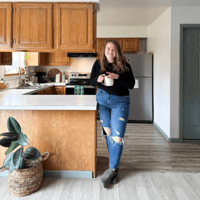 womans standing in a dark kitchen with oak cabinets and white countertops