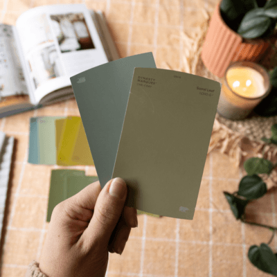 Hand holding green paint samples over a table