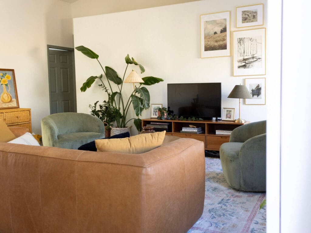 narrow living room with two green accent chairs, a long leather couch, and a tv stand with plans