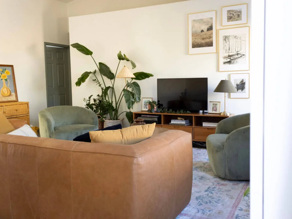 narrow living room with two green accent chairs, a long leather couch, and a tv stand with plans