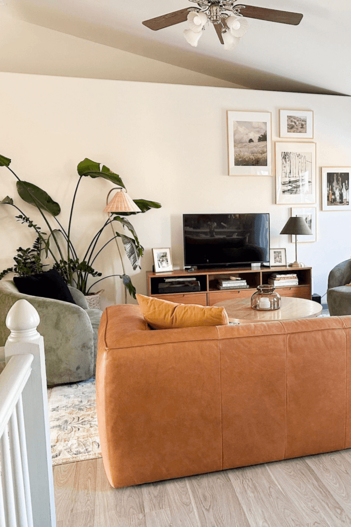 bright white narrow living room with green accent chairs, leather couch, gold gallery wall, and large plant