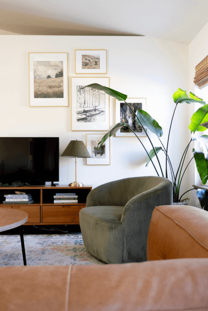 bright white narrow living room with green accent chair, leather couch, and gold gallery wall