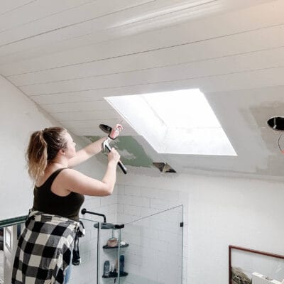 woman nailing in shiplap on a bathroom ceiling