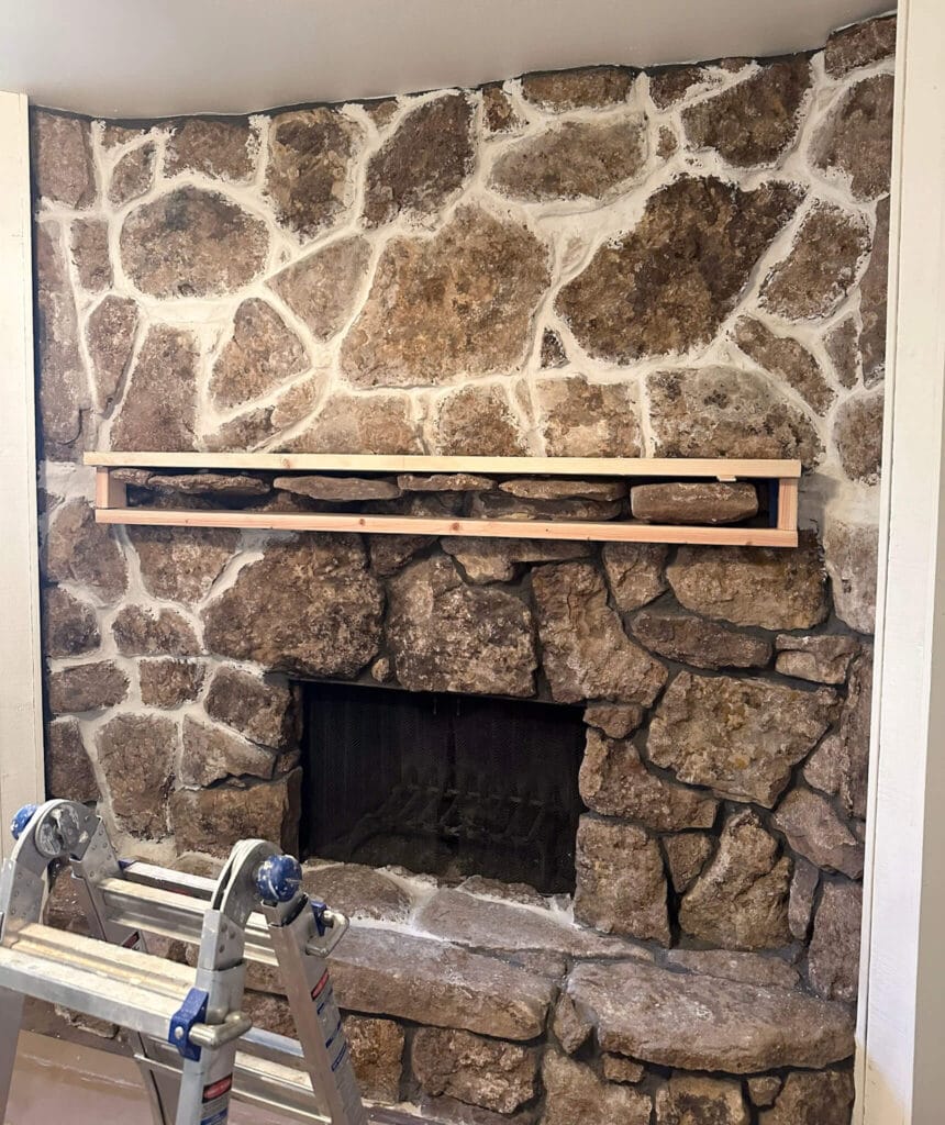 Stone fireplace during a renovation. Top half has new white mortar between the stones, and the bottom half has dark grout.