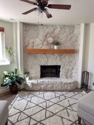 Painted white stone fireplace styled with geometric black and white rug, lavander pots, and a gold sun mirror on the mantel