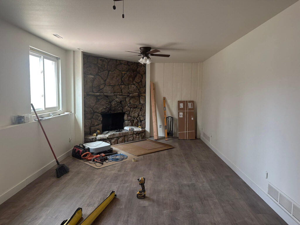 Old stone fireplace with gray/tan stone in a narrow living room being remodeled