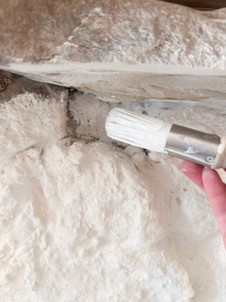 small white round brush held up next to a stone fireplace being painted white