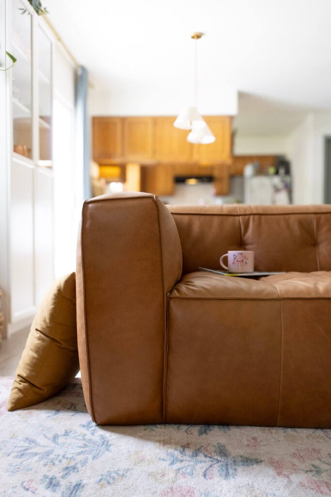 Capa cognac leather couch in an open, white living room with Rifle Paper Co floral rug