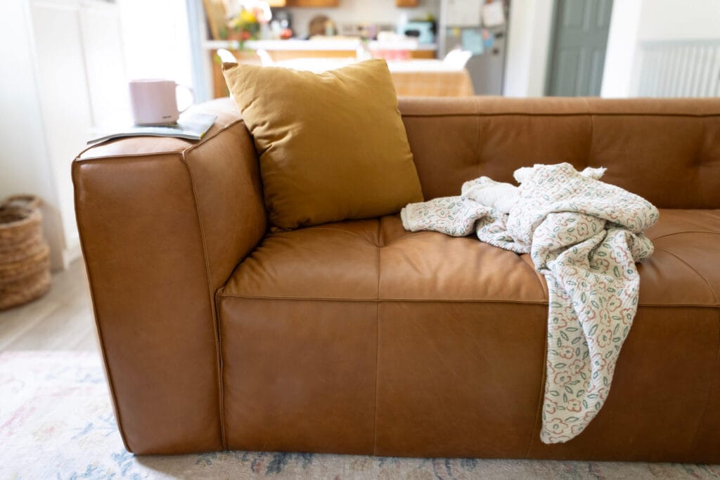 Leather cigar couch from Poly & Bark with gold pillow and white blanket in white living room